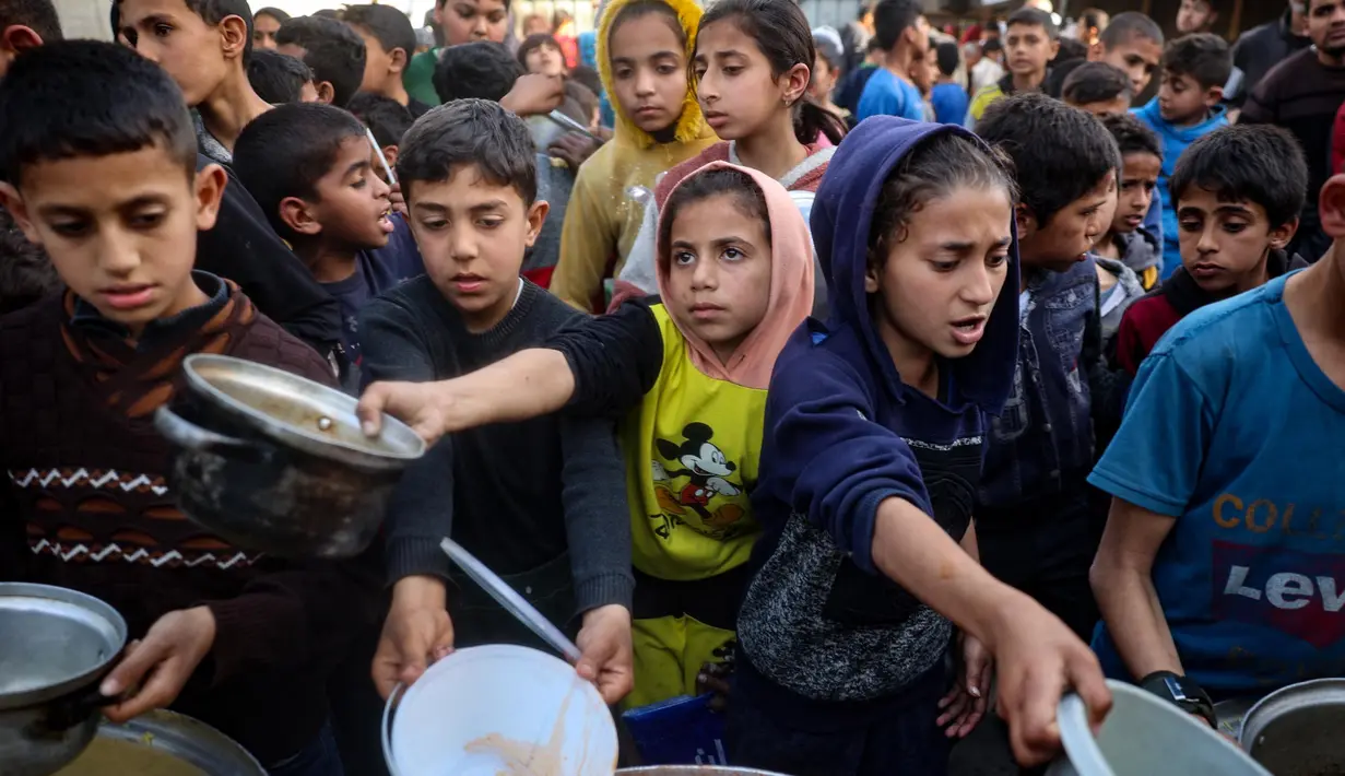 Anak-anak Palestina mendapatkan bagian dari makanan berbuka puasa untuk keluarga mereka di sebuah titik distribusi makanan gratis di kamp pengungsi Nuseirat, Jalur Gaza tengah, pada 14 Maret 2025. (Eyad BABA/AFP)