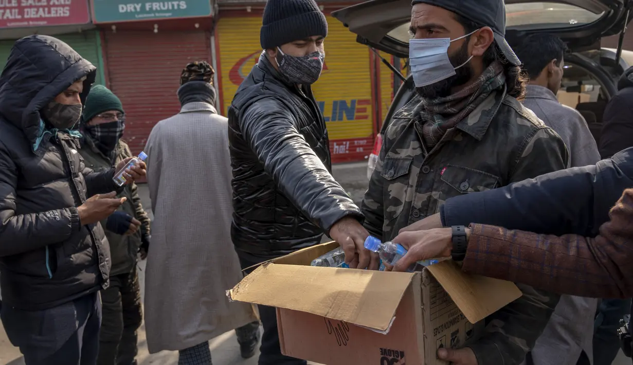Seorang pria membagikan botol pembersih selama penguncian akhir pekan di Srinagar, Kashmir yang dikuasai India, Sabtu (15/1/2022). Pihak berwenang di bagian Kashmir India mengumumkan pembatasan penuh pergerakan yang tidak penting selama akhir pekan  untuk mengekang COVID-19. (AP Photo/Dar Yasin)