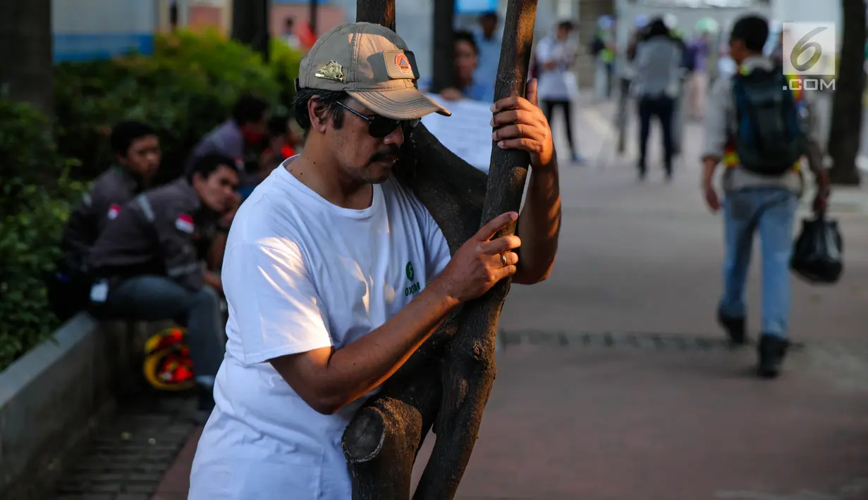 Seorang pria memeluk pohon saat menggelar aksi #ayopelukpohonini di Jalan Sudirman, Jakarta, Jumat (22/9). Aksi tersebut sebagai bentuk menyelamatkan pohon-pohon sepanjang Jalan Jenderal Sudirman dari proyek pelebaran trotoar. (Liputan6.com/Faizal Fanani)