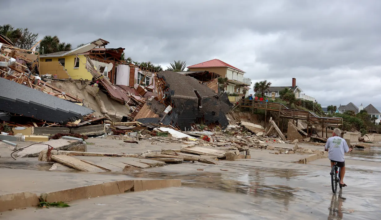 Seorang penduduk mengendarai sepedanya melewati rumah-rumah yang sebagian roboh ke pantai setelah Badai Nicole mendarat di Pantai Daytona, Florida (10/11/2022). Badai Nicoler datang ke darat sebagai badai Kategori 1 sebelum melemah menjadi badai tropis saat bergerak melintasi negara bagian. (Joe Raedle/Getty Images/AFP)