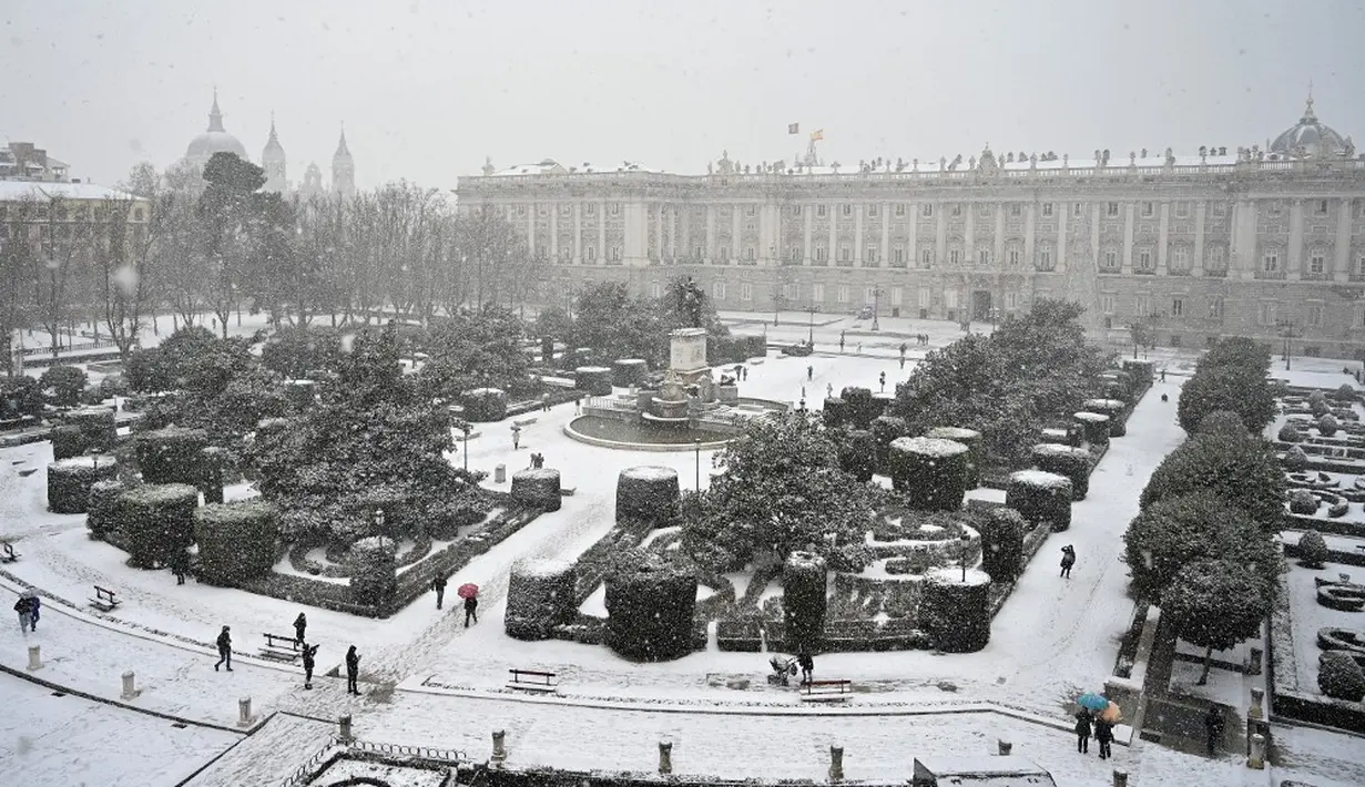 Orang-orang berjalan melewati salju di luar Istana Kerajaan, Madrid, Spanyol, Jumat (8/1/2021). Badai Filomena mengakibatkan salju lebat turun di Madrid dan seluruh Spanyol. (GABRIEL BOUYS/AFP)