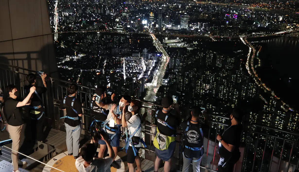 Pengunjung memakai masker untuk melindungi dari penyebaran Covid-19, berselfie saat menginap di lokasi perkemahan semalam di atap gedung pencakar langit di Seoul, Korea Selatan (7/8/2020). Menara Lotte World, setinggi 555 meter gedung pencakar langit dengan 123 lantai. (AP Photo/Lee Jin-man)
