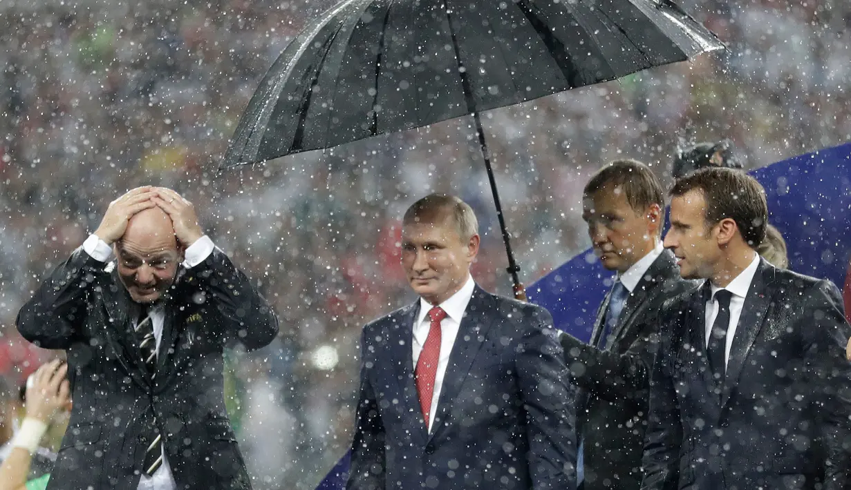 Presiden FIFA Gianni Infantino menutupi kepalanya dengan tangan sementara Presiden Rusia, Vladimir Putin dilindungi payung saat hujan turun selama penyerahan medali dan trofi Piala Dunia 2018 di Stadion Luzhniki, Minggu (15/7). (AP/Matthias Schrader)