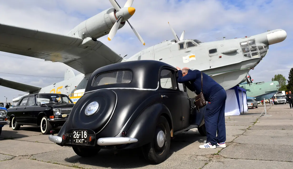 Seorang pengunjung melihat ke mobil di sebelah pesawat selama hari pembukaan festival mobil retro OldCarLand di Kiev (27/4). Pameran kendaraan jadul ini digelar dari 27 April hingga Mei, 1, 2018. (AFP Photo/Sergei Supinsky)