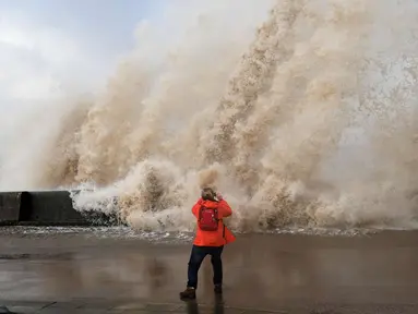 Seorang wanita mengambil gambar ombak yang disebabkan badai Eleanor di sepanjang pinggir laut di New Brighton, Inggris barat laut (3/1). Setelah melanda Inggris, badai Eleanor bergerak ke Prancis, Belgia dan Belanda. (AFP Photo/Paul Ellis)