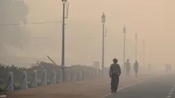Warga berjalan di dekat monumen India Gate yang diselimuti asap tebal di New Delhi, (20/10). Sehari usai perayaan Festival Diwali, polusi udara parah menyelimuti New Delhi dan beberapa kota di India. (AFP Photo/Dominique Faget)