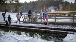 Seorang wanita mengeringkan dengan handuk setelah mandi di air es danau dekat Vilnius, Lithuania, Minggu (13/2/2022). Suhu udara 0 derajat Celcius (32 derajat Fahrenheit). (AP Photo/Mindaugas Kulbis)