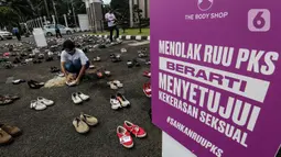 Pegiat komnas perempuan merapikan sepatu saat aksi diam 500 Langkah Awal Sahkan RUU PKS di depan gedung DPR, Jakarta, Rabu (25/11/2020). Dalam aksinya mereka menyusun sepatu sebagai simbol "semua peduli, semua terlindungi, stop sexual violence". (Liputan6.com/Johan Tallo)