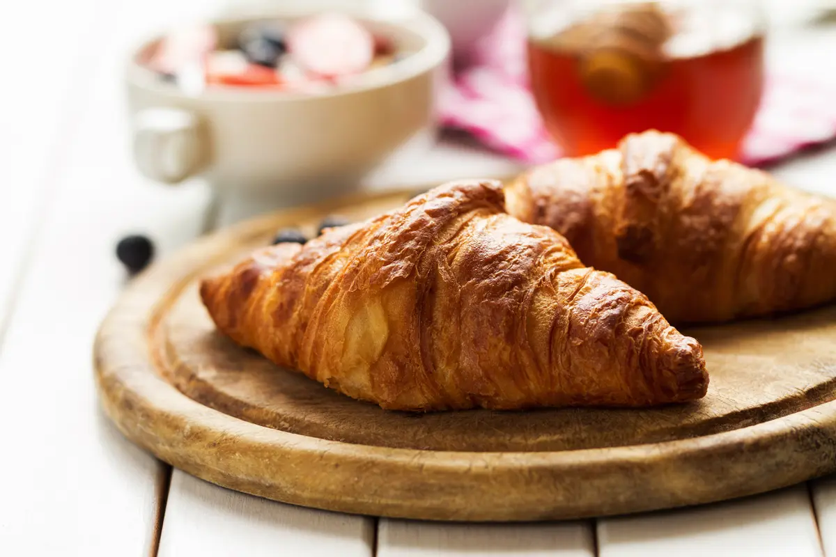 Dua buah croissant di atas sebuah piring berbahan kayu (Foto Dok: Freepik/valeria_aksakova)