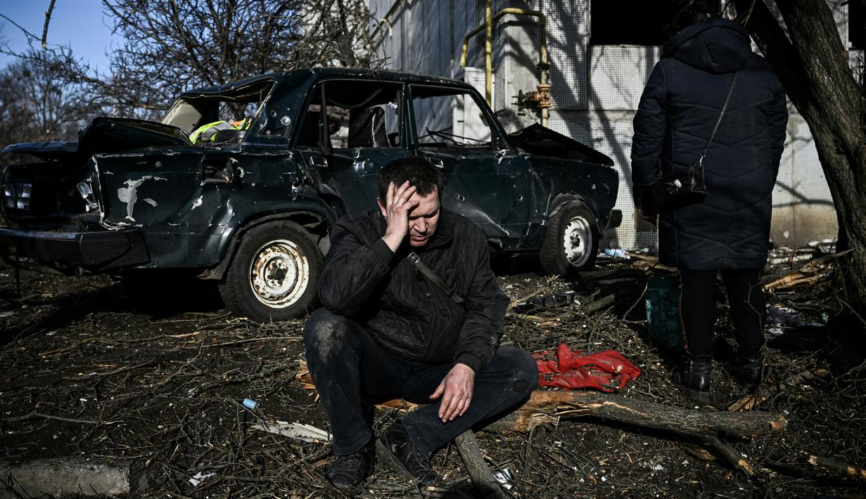 Seorang pria duduk di luar gedungnya yang hancur setelah pemboman di Kota Chuguiv, Ukraina timur, 24 Februari 2022. Angkatan bersenjata Rusia mencoba menyerang Ukraina dari beberapa arah, menggunakan sistem roket dan helikopter untuk menyerang posisi Ukraina di selatan. (Aris Messinis/AFP)