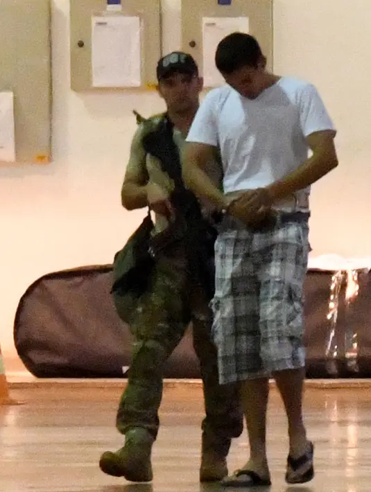 Terduga teroris berjalan dikawal oleh polisi di hanggar Polisi Federal Brasil di bandara di Brasil, (21/7). Kepolisan Brasil menangkap 10 orang amatiran yang disebut seakan-akan telah menyatakan kesetiannya kepada ISIS.( AFP PHOTO/Evaristo SA)