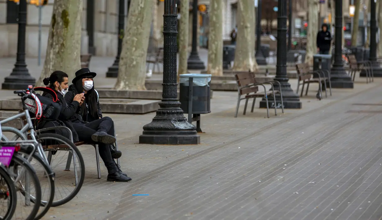Warga mengenakan masker duduk di pusat Kota Barcelona, Spanyol, Minggu (15/3/2020). Selama lockdown mengantisipasi penyebaran virus corona COVID-19, warga Spanyol dilarang meninggalkan rumah kecuali untuk membeli makanan, obat-obatan, bekerja, atau keadaan darurat. (AP Photo/Emilio Morenatti)