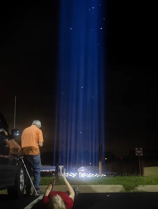 Orang-orang melihat pertunjukan cahaya saat mengunjungi penghormatan ringan untuk serangan 9/11 di Pentagon di Arlington, Virginia (10/9/2020). Pertunjukan tersebut adalah bagian dari peringatan skala kecil tahun ini karena pandemi virus corona. (Tasos Katopodis / Getty Images / AFP)