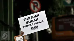 Aktivis dari Komunitas Pejalan Kaki membawa papan bertulis "TROTOAR BUKAN TEMPAT PARKIR" di Jakarta, Jum'at  (22/4). Mereka Menuntut kembalikan Trotoar untuk pejalan kaki sesuai dengan fungsinya dan membangun trotoar yang layak. (Liputan6.com/JohanTallo)