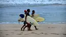 Anak-anak berjalan dengan papan selancar mereka di pantai Kuta di pulau resor Bali (4/10/2021). Pemerintah akan menyiapkan hotel-hotel yang dipersiapkan untuk karantina. (AFP/Sony Tumbelaka)