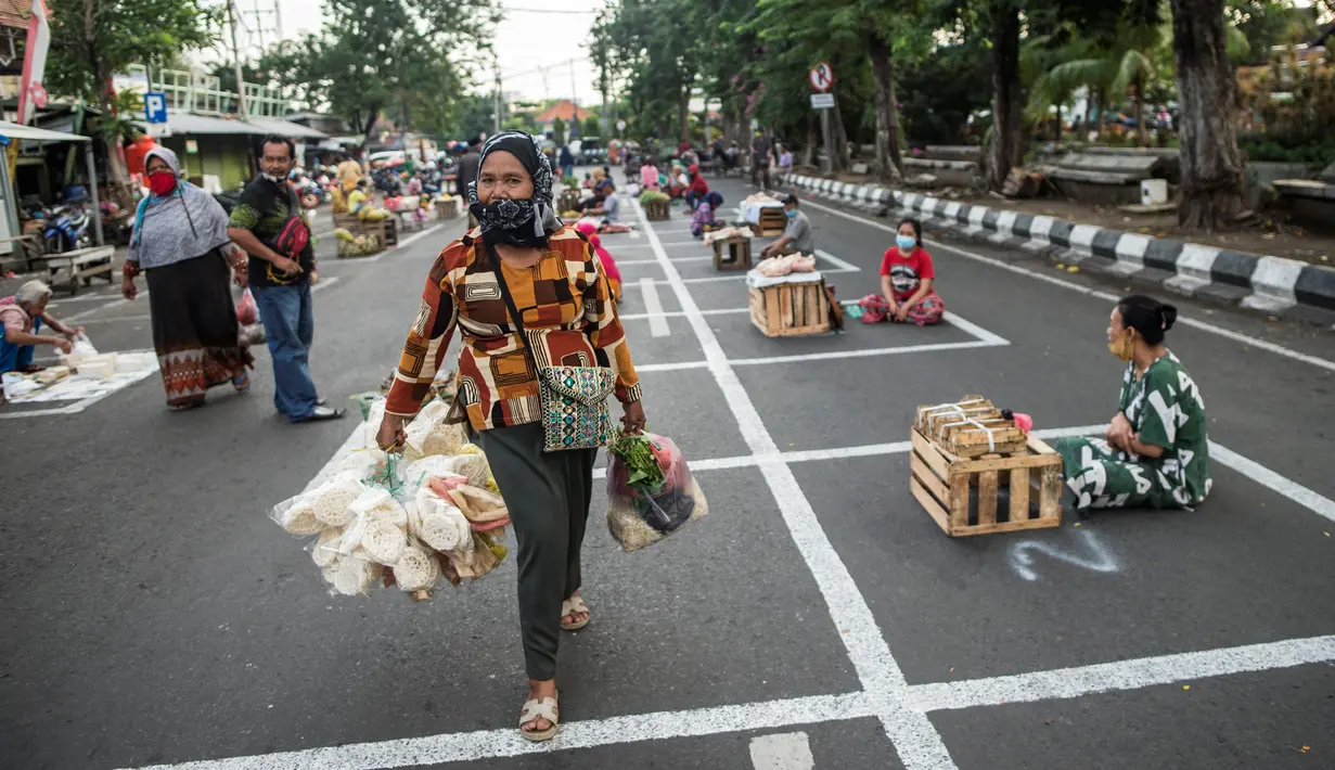 Warga melintasi pedagang yang  sedang menunggu pembeli di dalam garis petak-petak untuk menerapkan jaga jarak (physical distancing) di sepanjang jalan di Surabaya, Selasa (2/6/2020). Garis petak-petak bagi pedagang itu sebagai langkah pencegahan penyebaran COVID-19. (Photo by Juni Kriswanto / AFP)