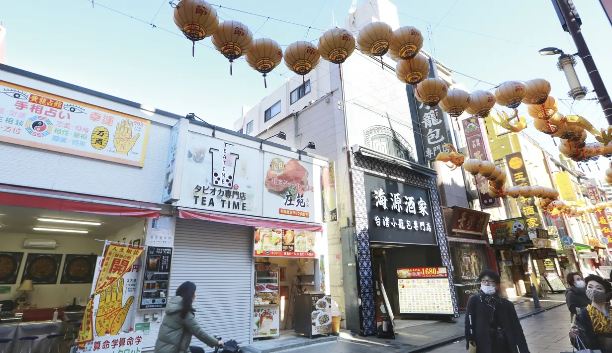 Orang-orang yang memakai masker berjalan di bawah pernak-pernik Imlek saat melintasi Chinatown di Yokohama, Prefektur Kanagawa, dekat Tokyo, Selasa (9/2/2021). Suasana Chinatown menjadi semakin meriah ketika Tahun Baru Imlek. (AP Photo/Koji Sasahara)
