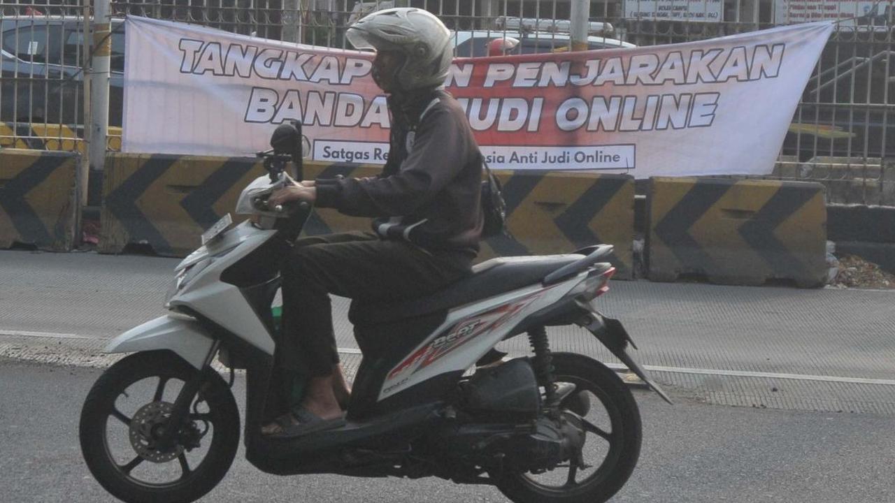 Pengendara melintas di dekat spanduk 'Tangkap dan Penjarakan Bandar Judi Online' yang terpampang di kawasan Mampang, Jakarta, Kamis (1/8/2024). Spanduk tersebut menyuarakan keresahan masyarakat terhadap menjamurnya praktik judi online. Foto: Merdeka.com/I