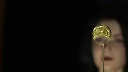 Seorang anggota staf berpose di sebelah bros emas dari Shropshire, Inggris. 1000 SM, dipamerkan di pameran The World of Stonehenge' di British Museum di London, Senin (14/2/2022). (AP Photo/Alastair Grant)