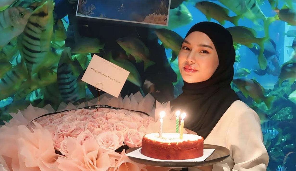 Dara Arafah mendapatkan kejutan dari sahabatnya di Sea World. Berfoto sembari memegang kue ulang tahun dan buket dengan latar belakangan pemandangan ikan, kebahagiaan terpancar jelas di wajah Dara Arafah. Dara Arafah tampil simpel tapi anggun dengan mengenakan blouse warna putih kemudian dipadukan dengan bawahan dan jilbab warna hitam. (Liputan6.com/IG/@daraarafah)