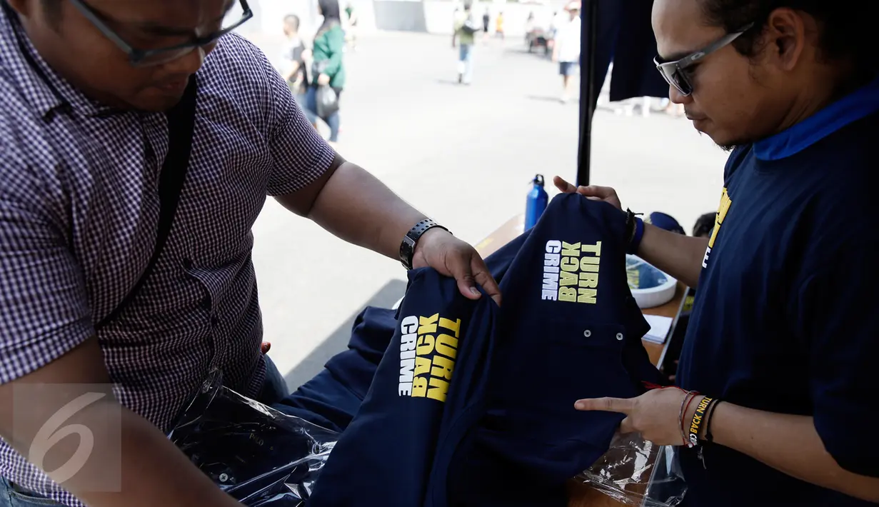 Calon pembeli melihat baju bertulisan "Turn Back Crime" yang dijual saat Car Free Day dikawasan Bunderan HI, Jakarta, Minggu (13/3). Penggunaan merk 'Turn Back Crime' bertujuan untuk kampanye waspada tindak kejahatan. (Liputan6.com/Faizal Fanani)