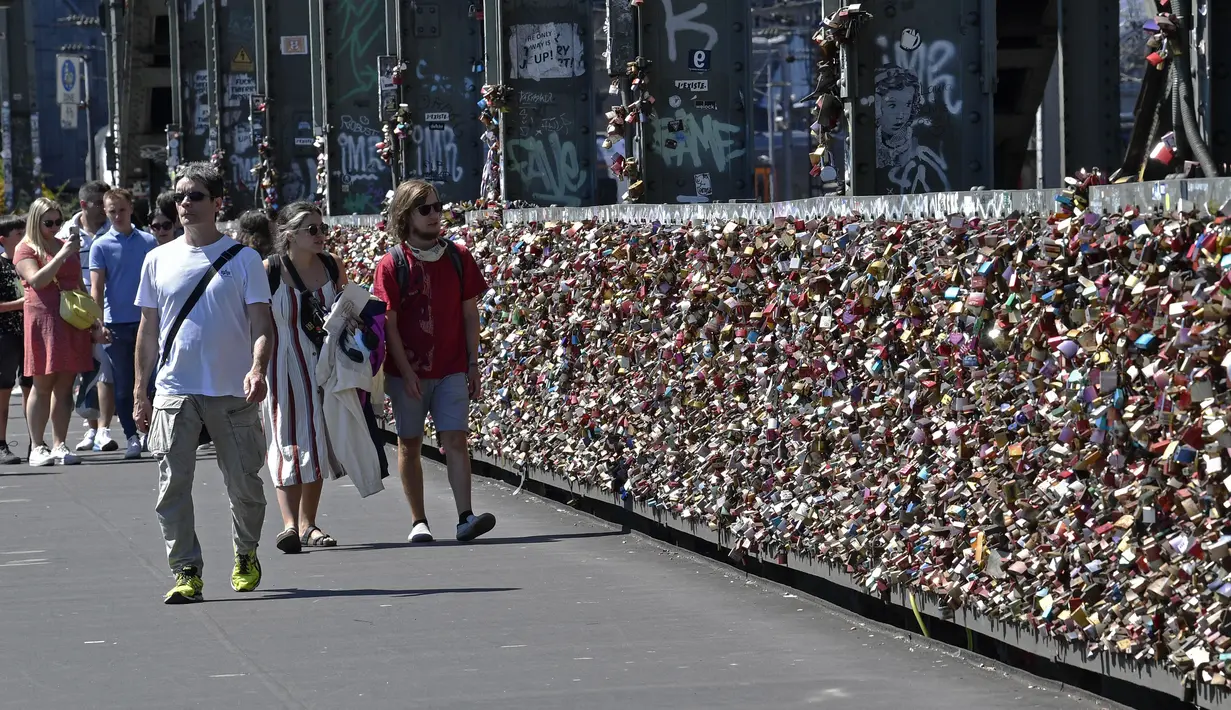 Warga melewati gembok cinta di sebuah jembatan di Cologne, Jerman, Rabu, (5/8/2020). Sebagai bukti cinta mereka, puluhan ribu pasangan telah memasang gembok selama bertahun-tahun ke pagar di Jembatan Hohenzollern sebelum melemparkan kunci ke dalam Sungai Rhein di bawah. (AP Photo/ Martin Meissner)
