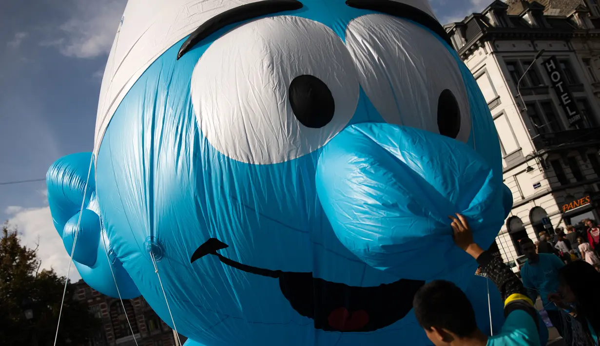 Sukarelawan memegang balon raksasa berbentuk karakter tokoh komik The Smurfs selama parade Comic Strip Festival di Brussels, Belgia, 15 September 2018. Tokoh komik terkenal dan karakter tokoh Belgia ditampilkan sepanjang jalan. (AP Photo/Francisco Seco)