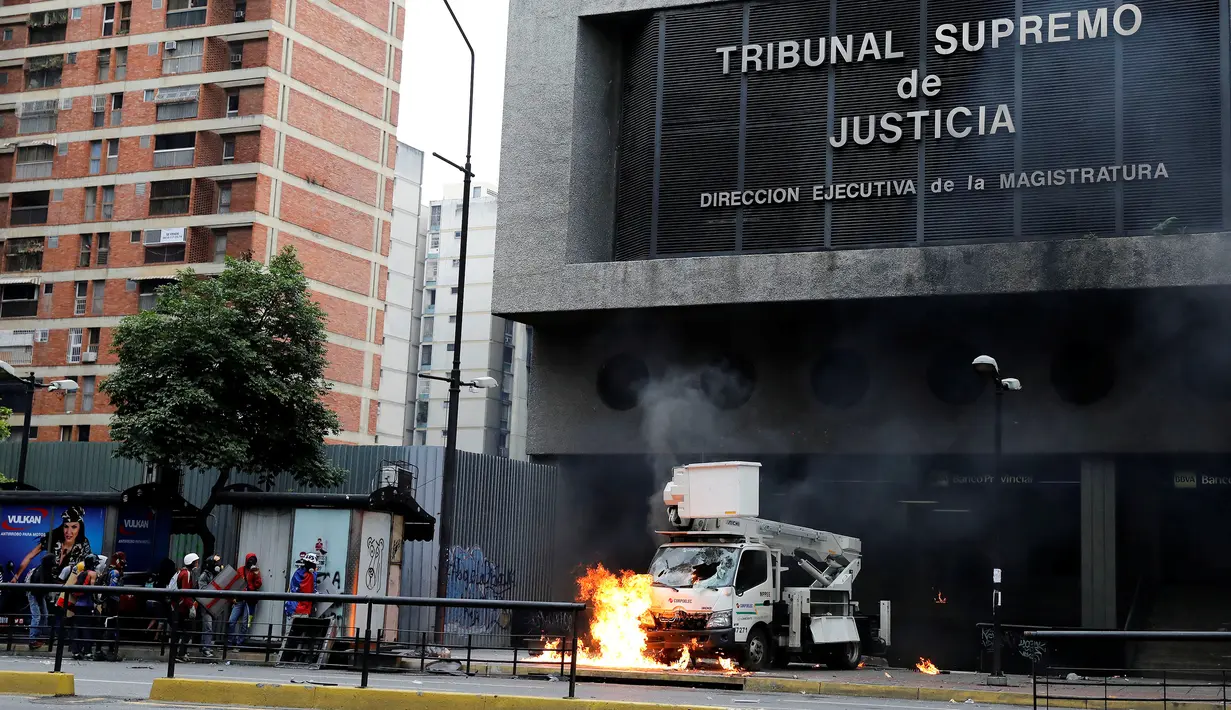 Suasana kerusuhan di depan Gedung Pengadilan Tinggi Venezuela menuntut Presiden Nicolas Maduro di Caracas (7/6).  Para demonstran menghancurkan dan membakar sebuah kendaraan yang terparkir di depan gedung. (Reuters/Carlos Garcia Rawlins)