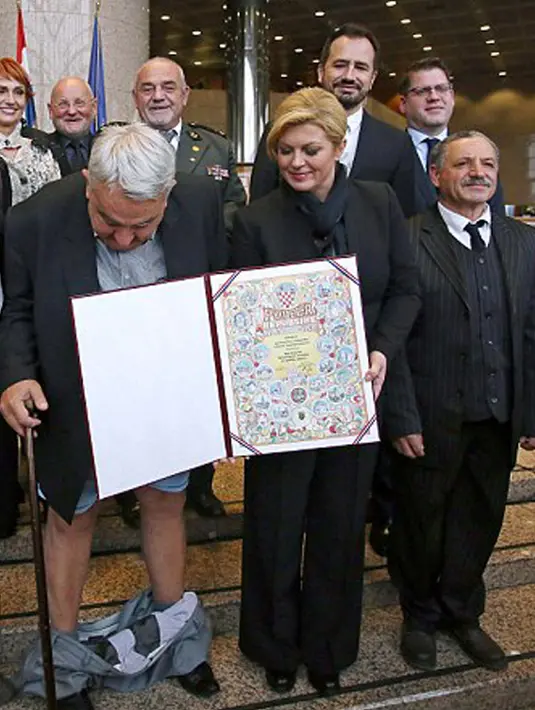 Kejadian memalukan saat celana panjang Kepala Komisi HAM Helsinki Kroasia, Ivan Zvonimir Cicak melorot hingga ke pergelangan kakinya tepat saat sesi foto dengan Presiden Kroasia Kolinda Grabar-Kitrarovic di Zagreb, Selasa (8/12). (dailymail.co.uk)