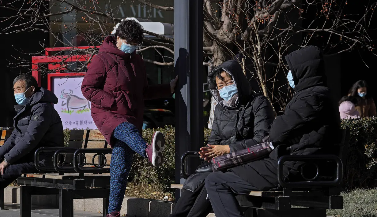 Seorang wanita mengenakan masker untuk melindungi diri dari virus corona berjalan di atas papan yang menampilkan Bing Dwen Dwen, maskot Olimpiade Musim Dingin 2022, di Beijing, Minggu (12/12/2021). (AP Photo/Andy Wong)