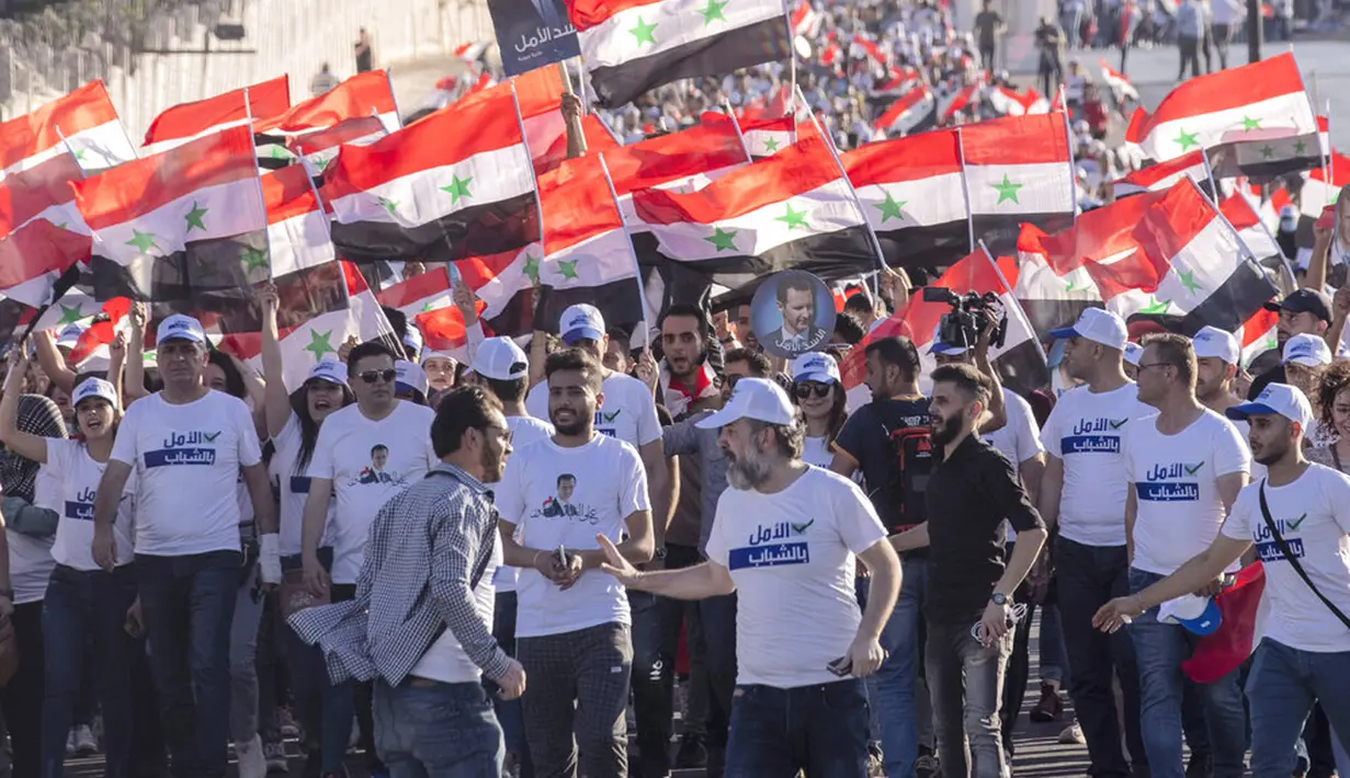 Pendukung Presiden Suriah Bashar Assad mengibarkan bendera nasional Suriah dan foto-foto Assad pada pertemuan di Omayyid Square, Damaskus, Suriah, Minggu (23/5/2021). Pemilihan presiden di negara yang dilanda perang itu akan diadakan pada 26 Mei. (AP Photo/Hassan Ammar)
