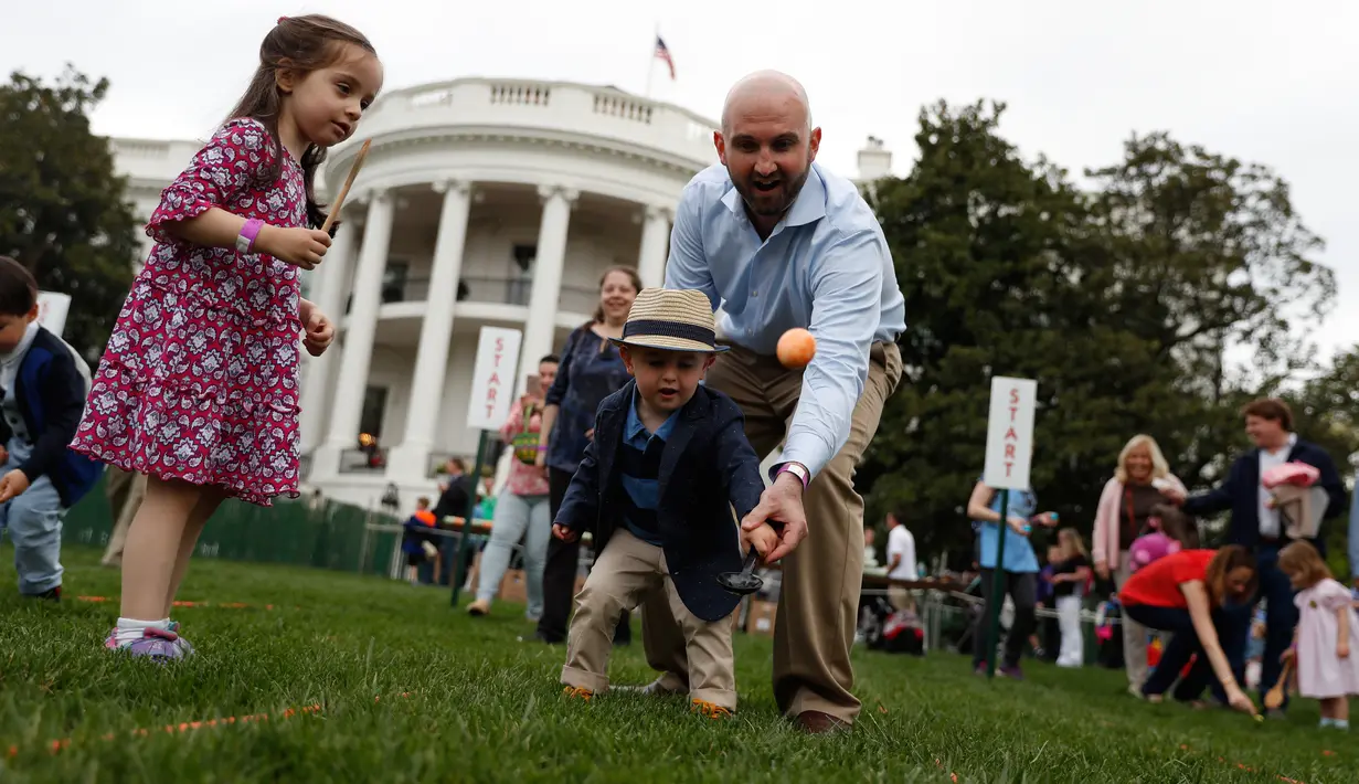 Seorang pria membantu anaknya menggelindingkan telur saat lomba perayaan Paskah di halaman Gedung Putih, Washington, Senin (17/4).Lomba yang diselenggarakan setiap tahunnya ini merupakan lomba menggelindingkan telur yang ke-139. (AP Photo/Carolyn Kaster)
