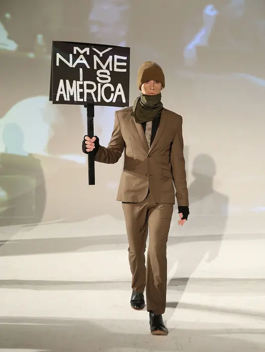 Seorang model membawa poster saat presentasi karya desainer Robert James dalam New York Fashion Week (NYFW) di New York,AS  (30/1). (Robin Marchant Getty Images/AFP)