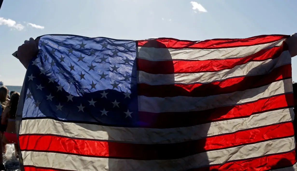 Perenang Polar Bear Club membawa bendera Amerika Serikat bersiap terjun ke air dingin pantai Samudera Atlantik di Coney Island, New York (1/1). Mereka berenang di pantai Samudera Atlantik dengan suhu 17 derajat Fahrenheit. (Yana Paskova/Getty Images/AFP)