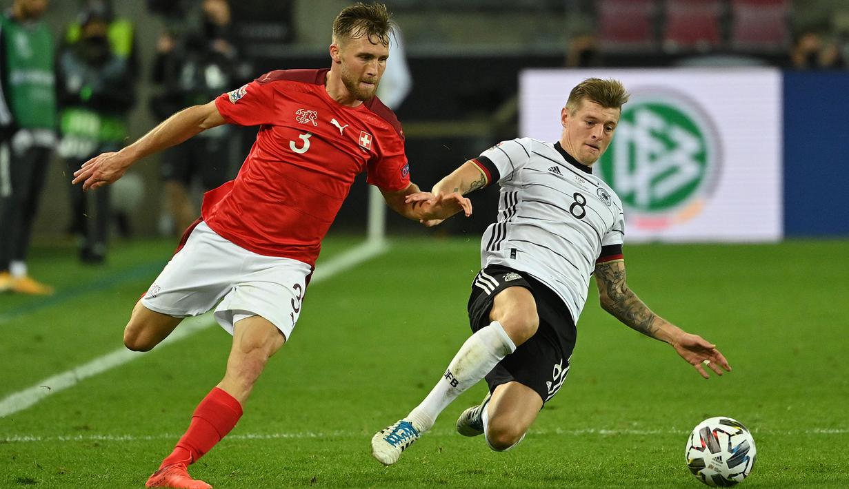 Gelandang Jerman, Toni Kroos, berebut bola dengan bek Swiss, Silvan Widmer, pada laga lanjutan UEFA Nations League 2020/2021 di RheinEnergie Stadion, Rabu (14/10/2020). Jerman bermain imbang 3-3 atas Swiss. (AFP/Ina Fassbender)