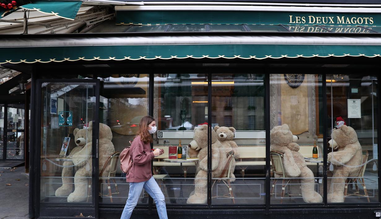 Pejalan kaki melintas di depan boneka beruang raksasa di kafe Les Deux Magots yang ditutup di Paris, Prancis, pada 16 Desember 2020. Boneka beruang itu dipajang untuk menggantikan pengunjung saat restoran tutup selama penerapan jam malam guna menekan laju penyebaran COVID-19. (Xinhua/Gao Jing)