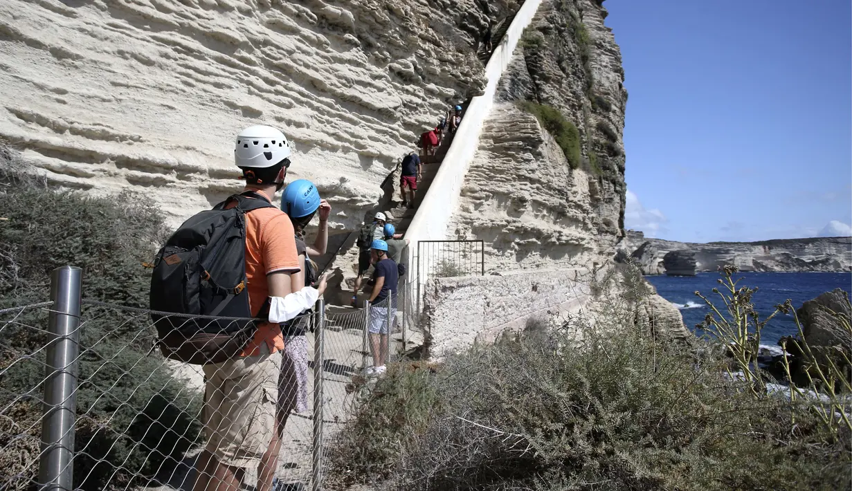 Turis menaiki tangga Raja Aragon di Bonifacio di pulau Corsica, Mediterania Prancis (19/9/2021). Pada kenyataannya, tangga itu digali oleh para biarawan Fransiskan untuk mengakses sumber air minum, yang tidak lagi digunakan. (AFP/Pascal Pochard-Casabianca)
