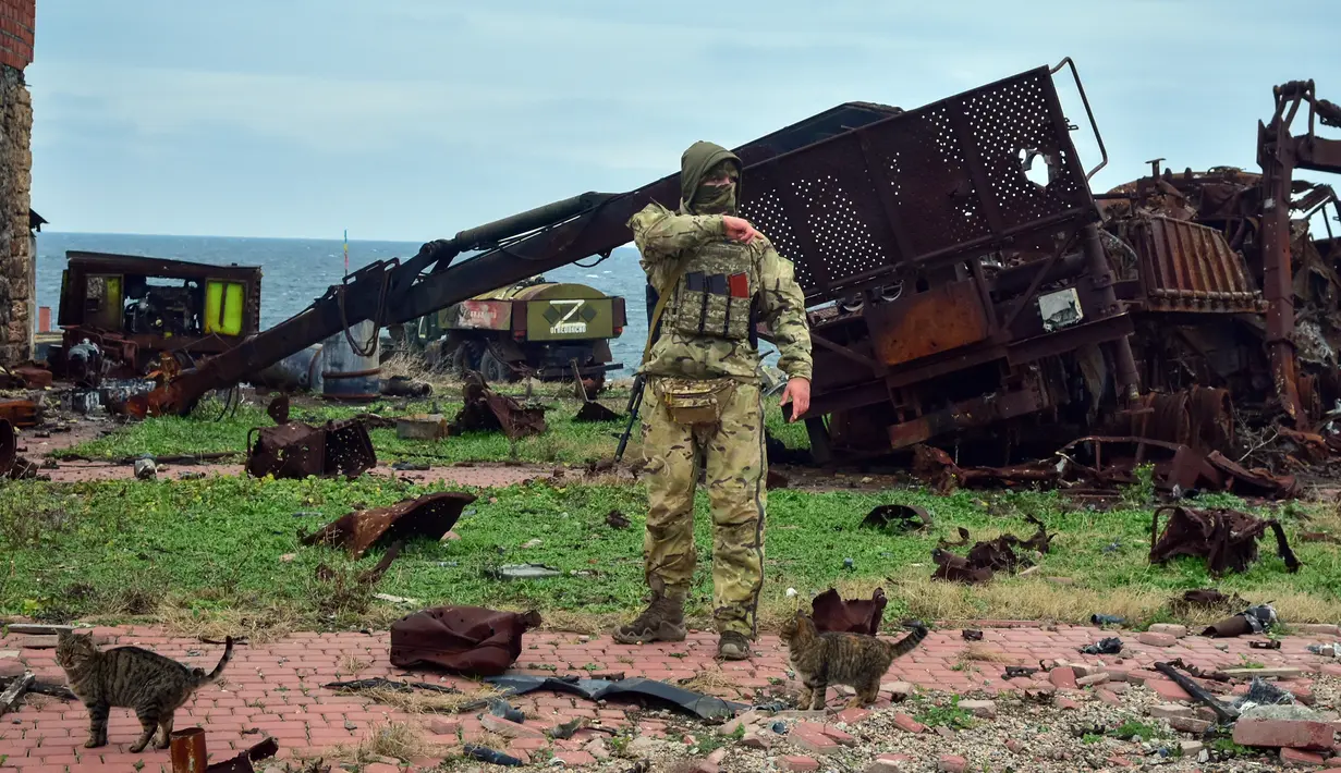 Seorang tentara Ukraina dan beberapa ekor kucing berdiri dengan latar belakang kendaraan militer Rusia yang rusak di Pulau Ular, Laut Hitam, Ukraina, 18 Desember 2022. Pasukan Rusia menduduki pulau itu pada awal-awal invasinya ke Ukraina, namun akhirnya mundur beberapa bulan kemudian. (AP Photo/Michael Shtekel)