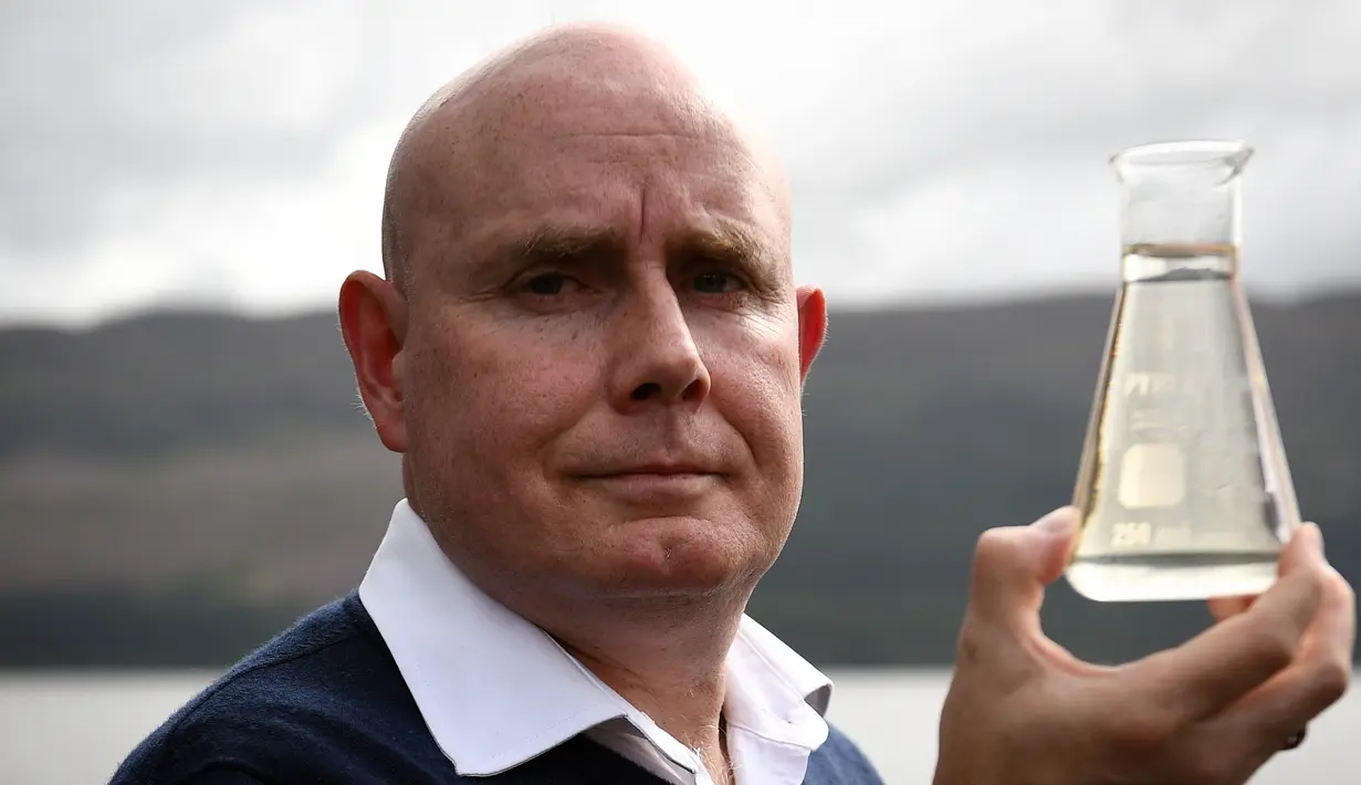 Ahli genetika Universitas Otago Profesor Neil Gemmell berpose dengan wadah air di perairan Loch Ness, Drumnadrochit, Skotlandia, Kamis (5/9/2019). Menurut Gemmell, monster legendaris Loch Ness yang diyakini orang kemungkinan adalah belut raksasa. (Andy Buchanan/AFP)