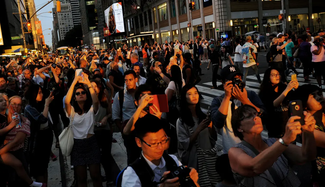 Sejumlah wisatawan mengabadikan fenomena Manhattanhenge di New York, AS, Senin (11/7). Matahari terbit dan terbenam dalam garis lurus di jalan utama Manhattan dan hanya terjadi  pada musim panas. (REUTERS)