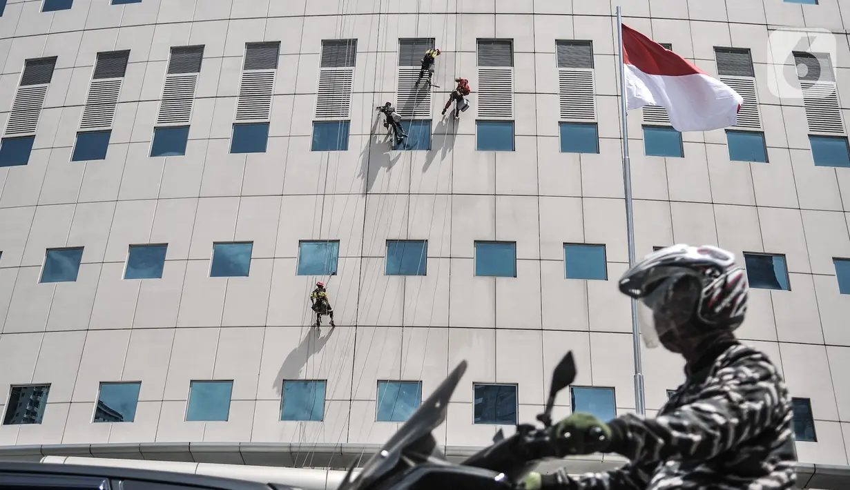 Pengendara motor melintas di bawah pekerja yang tengah melakukan perawatan gedung perkantoran di kawasan Sudirman, Jakarta, Senin (30/11/2020). (merdeka.com/Iqbal S. Nugroho)