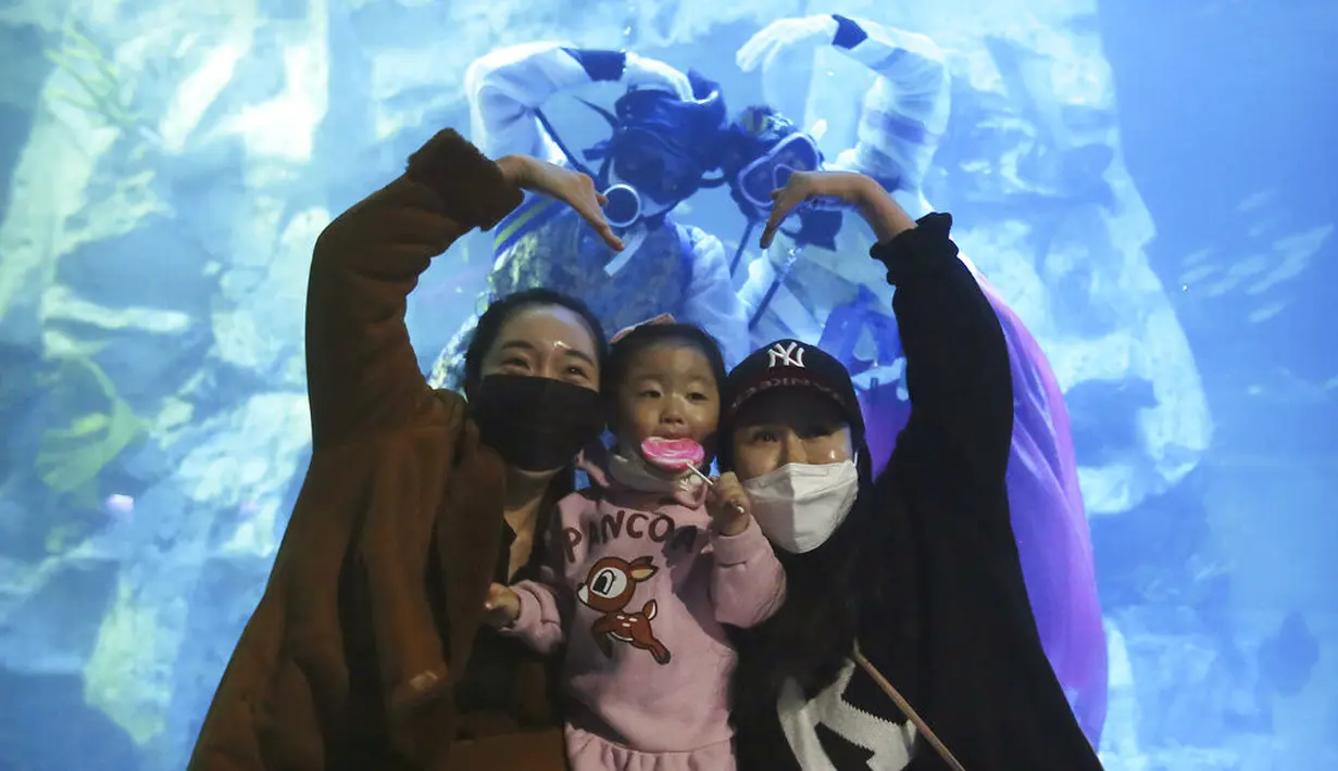 Pengunjung yang mengenakan masker untuk mencegah COVID-19 berpose dengan penyelam berkostum tradisional Korea saat perayaan Tahun Baru dalam akuarium di Seoul, Korea Selatan, Minggu (3/1/2021). (AP Photo/Ahn Young-joon)