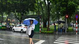 Seorang wanita melintasi jalan saat hujan lebat di Hanoi (14/10/2020). Badai tropis Nangka menghantam Vietnam tengah-utara yang mengakibatkan bencana alam, terutama hujan lebat dan banjir, telah menyebabkan 28 orang tewas dan 12 lainnya hilang. (AFP Photo/Manan Vatsyayana)
