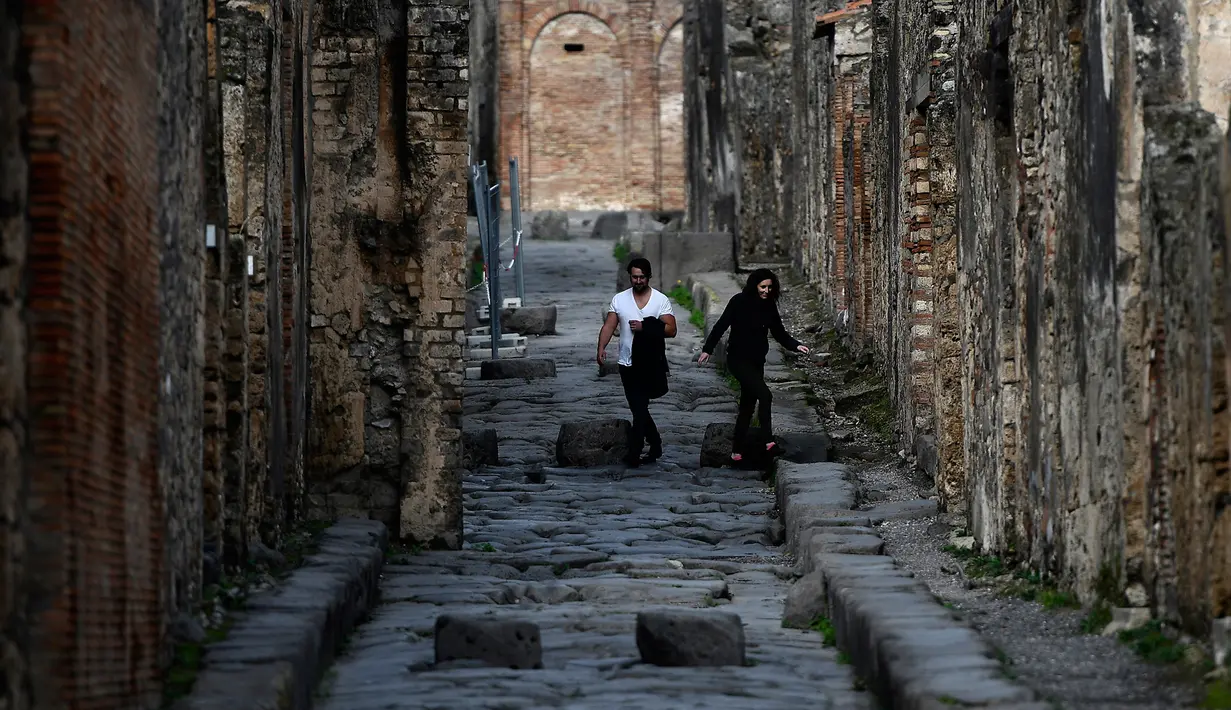 Wisatawan berjalan di gang berbatu, Pompeii, Italia, Senin (25/11/2019). Sisa-sisa kehidupan di Kota Pompeii masih tetap bertahan hingga sekarang. (Filippo MONTEFORTE/AFP)