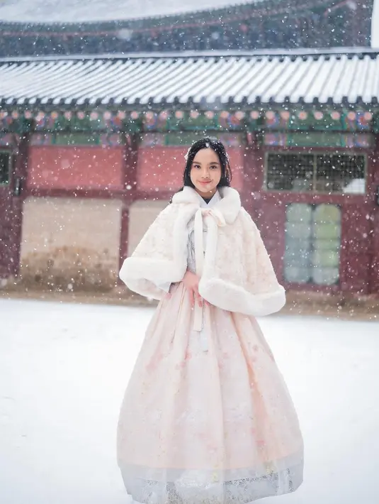 Ia mengenakan hanbok bernuansa peach berbalut cropped coat berbulu yang jadi outfit musim dingin [@lyodraofficial]