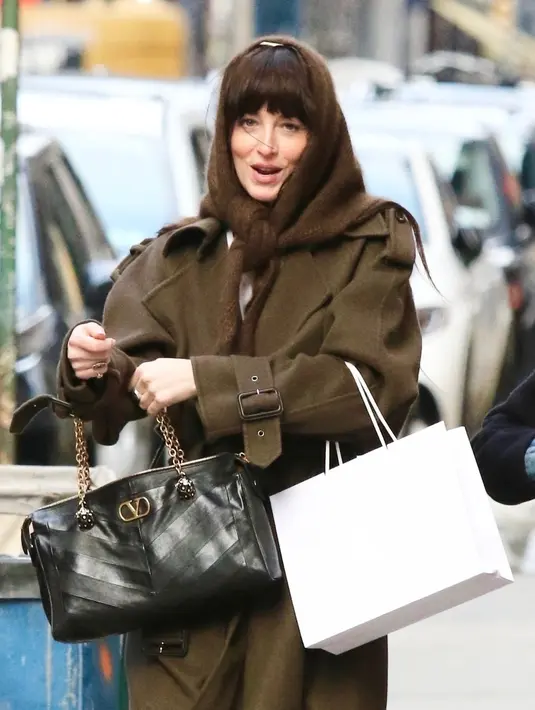 Dakota Johnshon tampil dengan long coat coklay senada dengan penutup kepalanya. Di tangannya ia membawa tas Valentino Garavani Panthea hitam yang telah menjadi pusat perhatian dalam koleksi Fireflies Spring Summer 2026. [Dok. Valentino]