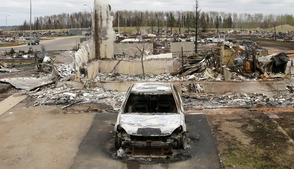 Sebuah kendaraan dan rumah terlihat hangus akibat kebakaran hutan di Beacon Hill dari Fort McMurray, Alberta, Kanada, (9/5). Sekitar 80 ribu warga Kanada terpaksa dievakuasi Akibat kebakaran dahsyat di seluruh kota ini. (REUTERS/Chris Wattie)