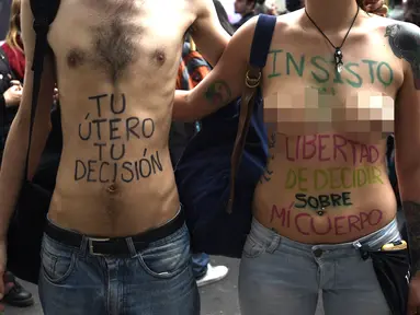 Sepasang demonstran bertelanjang dada saat menggelar aksi di Buenos Aires, Argentina (29/9). Dalam aksi ini badan mereka di cat dengan tulisan yang mengimbau bahwa rahim dan tubuh mereka kebebasan mereka. (AFP Photo/Juan Mabromata)