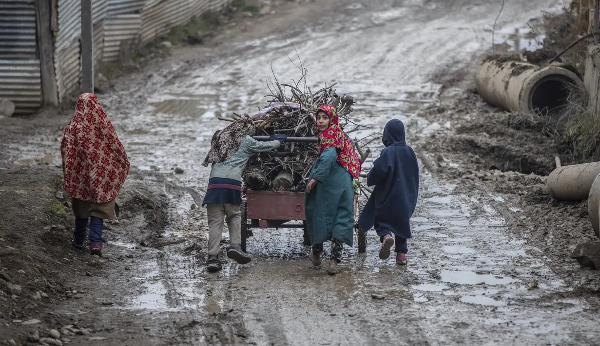 Anak-anak Kashmir mendorong gerobak berisi kayu bakar pada hari yang dingin di pinggiran Srinagar, Kashmir yang dikuasai India, Senin (27/12/2021). (AP Photo/Mukhtar Khan)