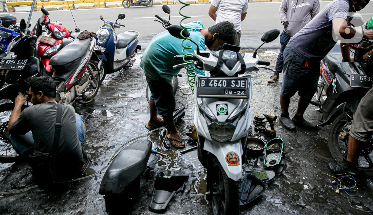 Montir membersihkan sepeda motor konsumen usai terendam banjir di kawasan Mampang, Jakarta, Minggu (21/2/2021). Banjir yang melanda Ibu Kota Jakarta pada Sabtu (20/2) menyebabkan banyak kendaraan warga mengalami kerusakan akibat terendam air. (Liputan6.com/Faizal Fanani)
